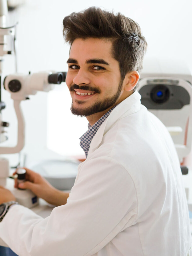 Óptico joven sonriendo mientras utiliza un equipo de diagnóstico en Óptica Giner.