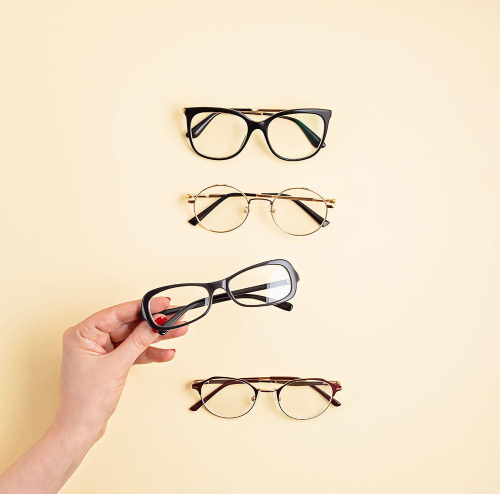 Variedad de gafas de diferentes estilos y una mano sujetando una montura, catálogo de Óptica Giner.