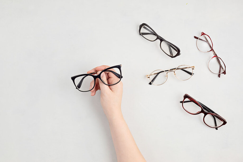 Mano eligiendo unas gafas entre varias monturas sobre fondo claro, colección de Óptica Giner.