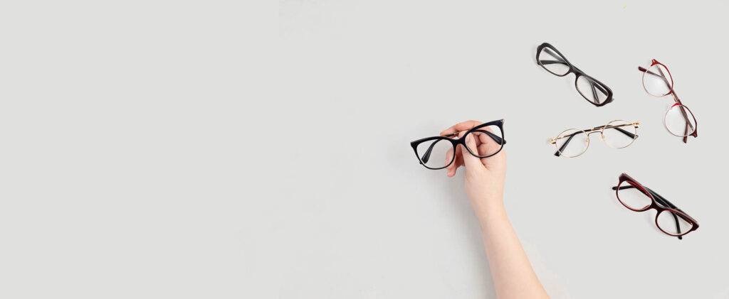 Mano eligiendo unas gafas entre varias monturas sobre fondo claro, colección de Óptica Giner.
